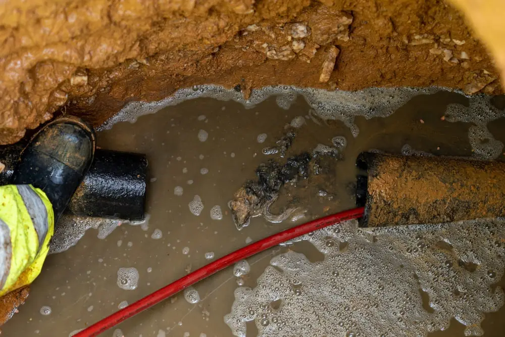 Débouchage canalisation à Arlon dans une tranchée boueuse avec canalisation obstruée et flexible rouge