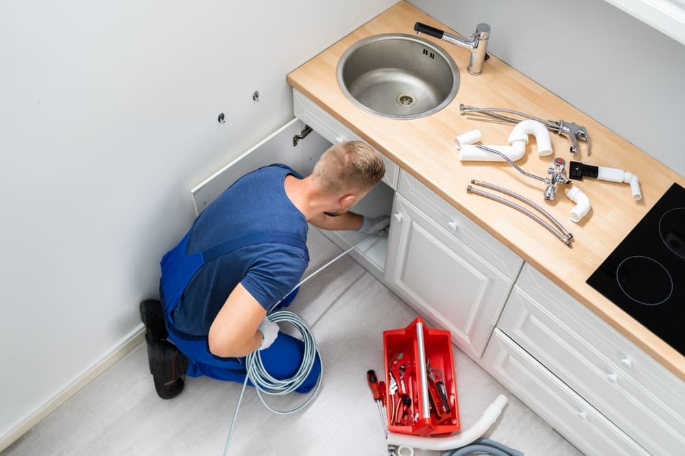 un professionnel de l'entreprise Mertens intervenant sur un évier bouché avec outils de débouchage évier, estimation du prix du service