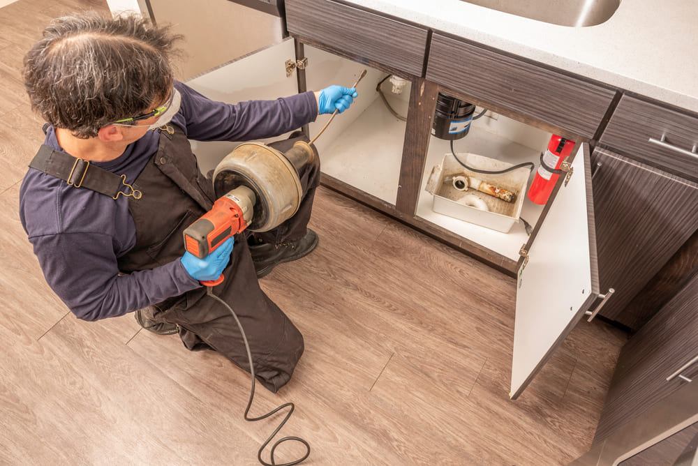 Technicien effectuant un débouchage de lavabo de cuisine avec une machine à câble